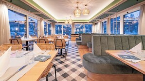 Un espace de restauration moderne avec un sol à carreaux, des tables en bois et des sièges rembourrés. De grandes fenêtres offrent une vue sur le paysage urbain.