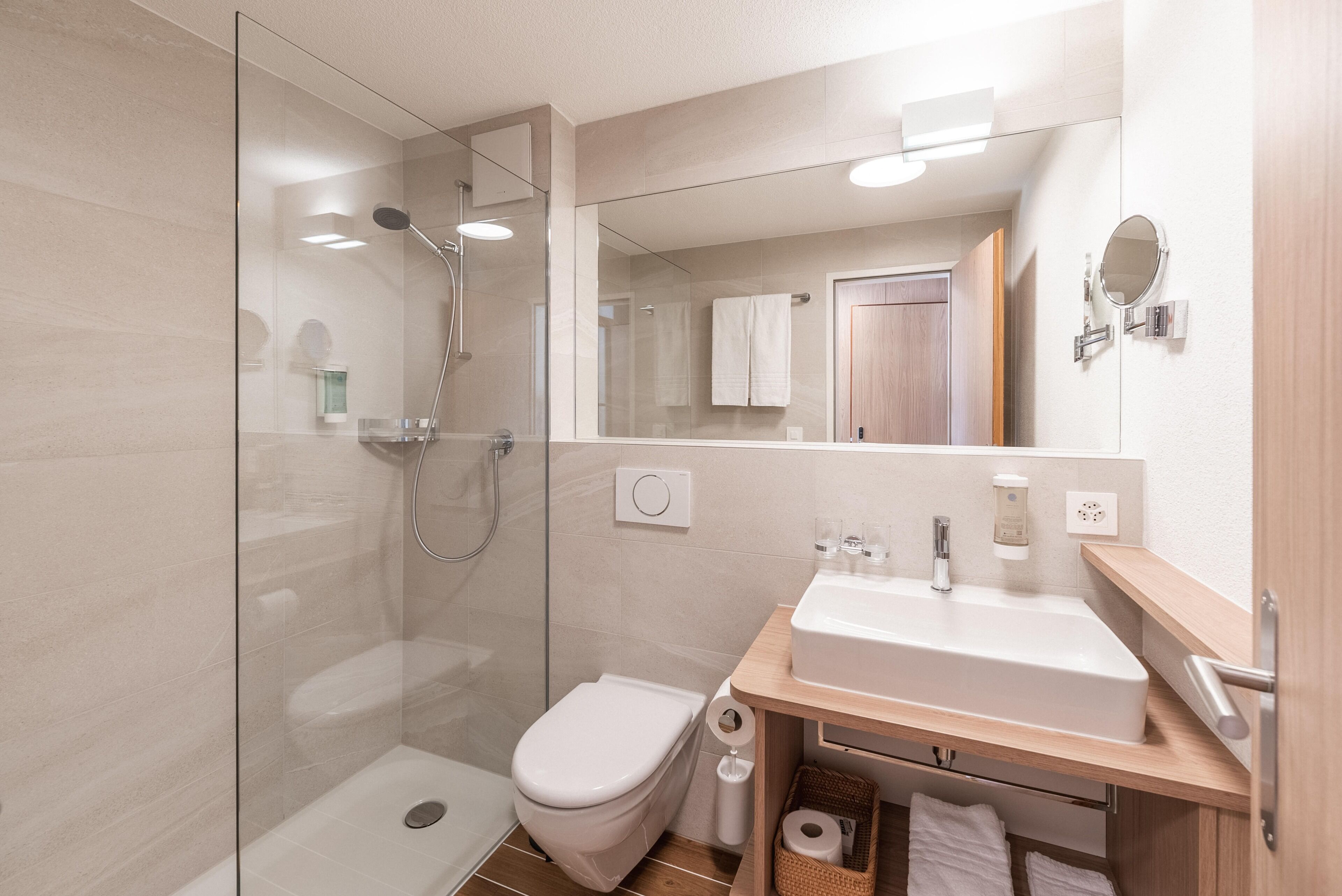 Ein modernes Badezimmer mit einer gläsernen Duschkabine, einer weißen Toilette, einem Waschbecken mit Spiegel und einer Holzausstattung.