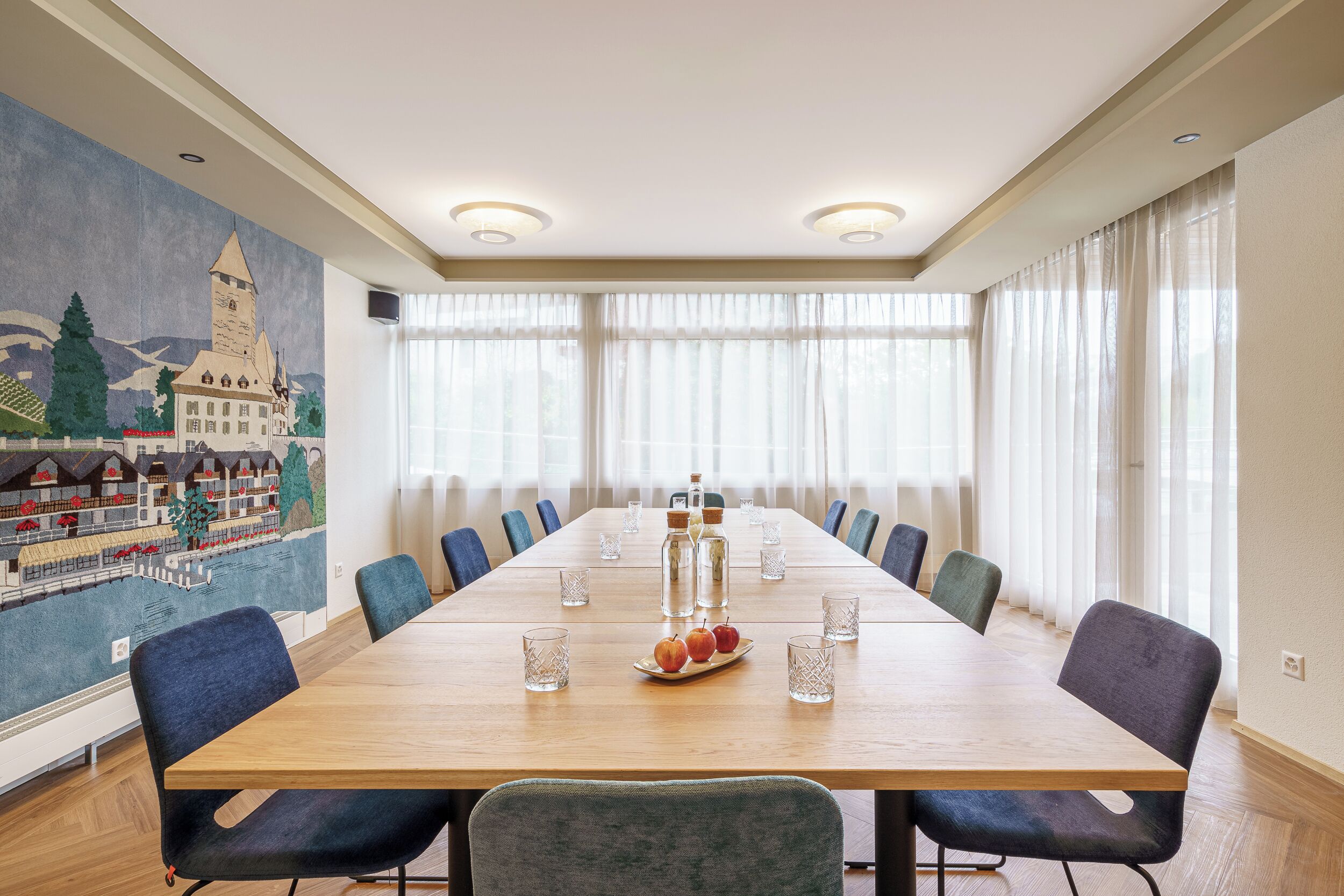 A conference room with a long table, chairs, and a mural of a town on the wall.