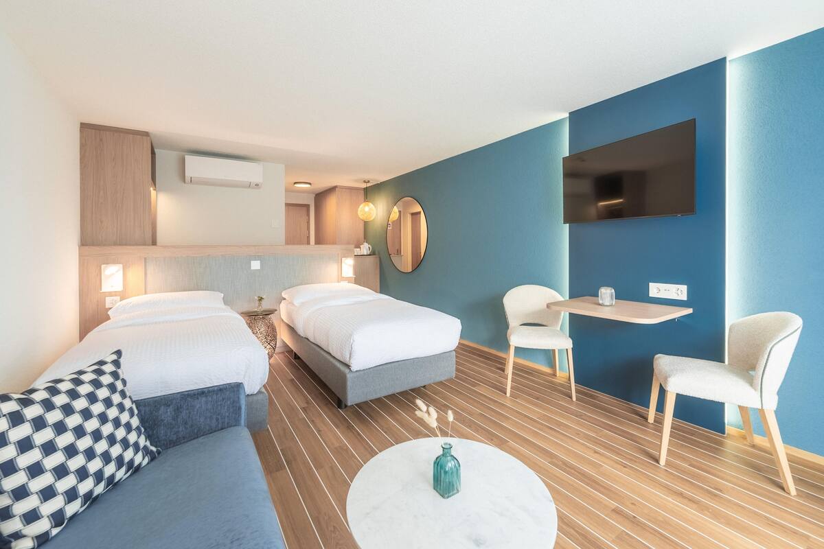 A modern hotel room with two beds, a sofa, a small table, and a TV.
