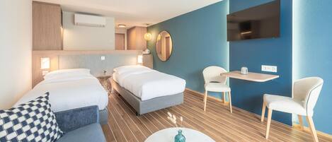 A modern hotel room with two beds, a sofa, a small table, and a TV.