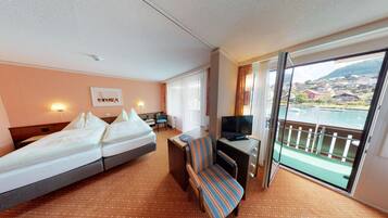 A hotel room with a bed, a desk with a chair, a television, and a large window offering a view of a body of water and buildings.