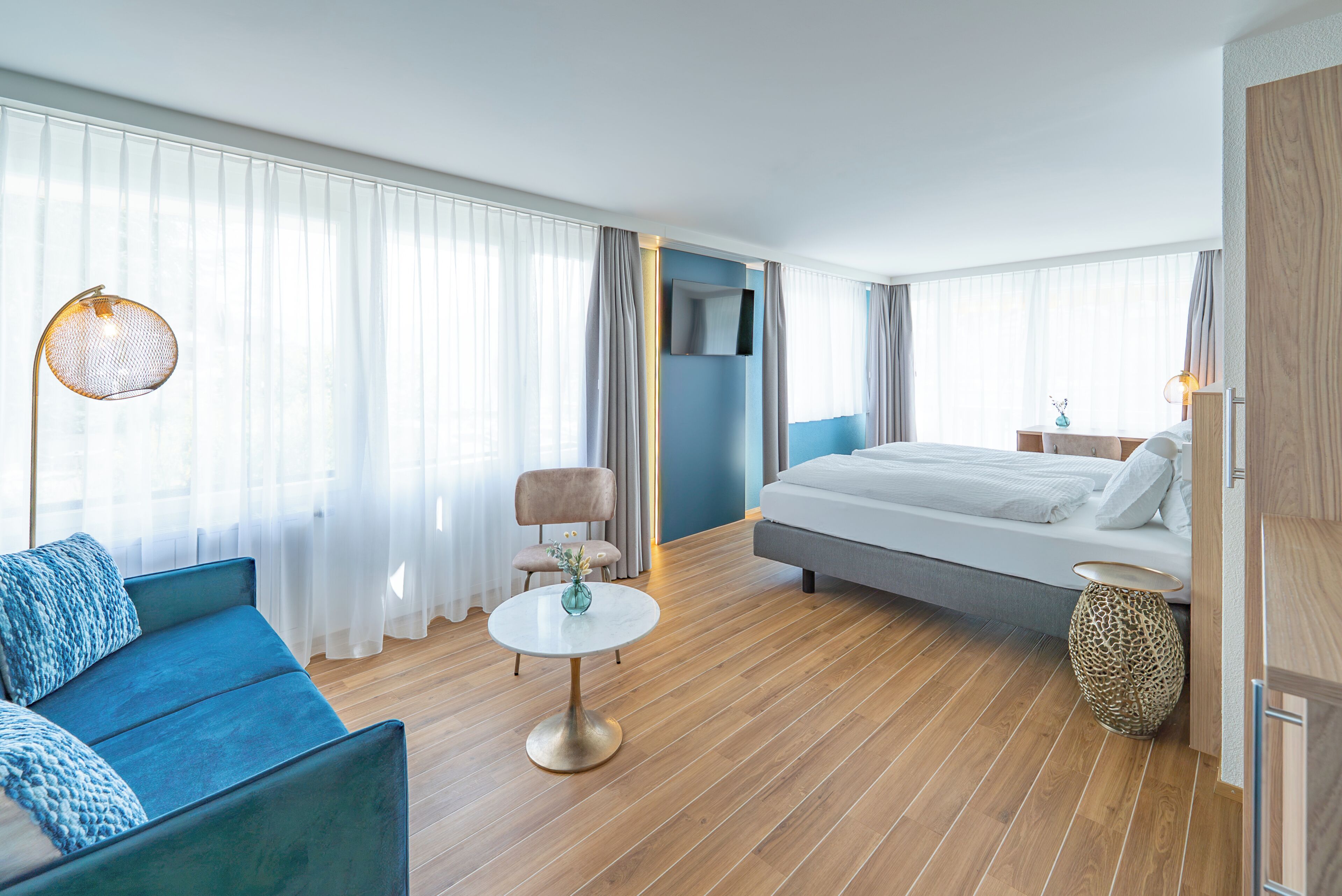 A modern hotel room with a bed, a sofa, a small table, and a chair.