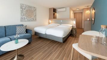 Ein modernes Hotelzimmer mit einem Bett, einem blauen Sofa, einem runden Couchtisch und einem Holzessttisch.