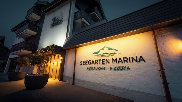 The exterior of Seegarten Marina restaurant and pizzeria with illuminated signage and potted plants. - Hotel-Restaurant Seegarten-Marina (Spiez)
