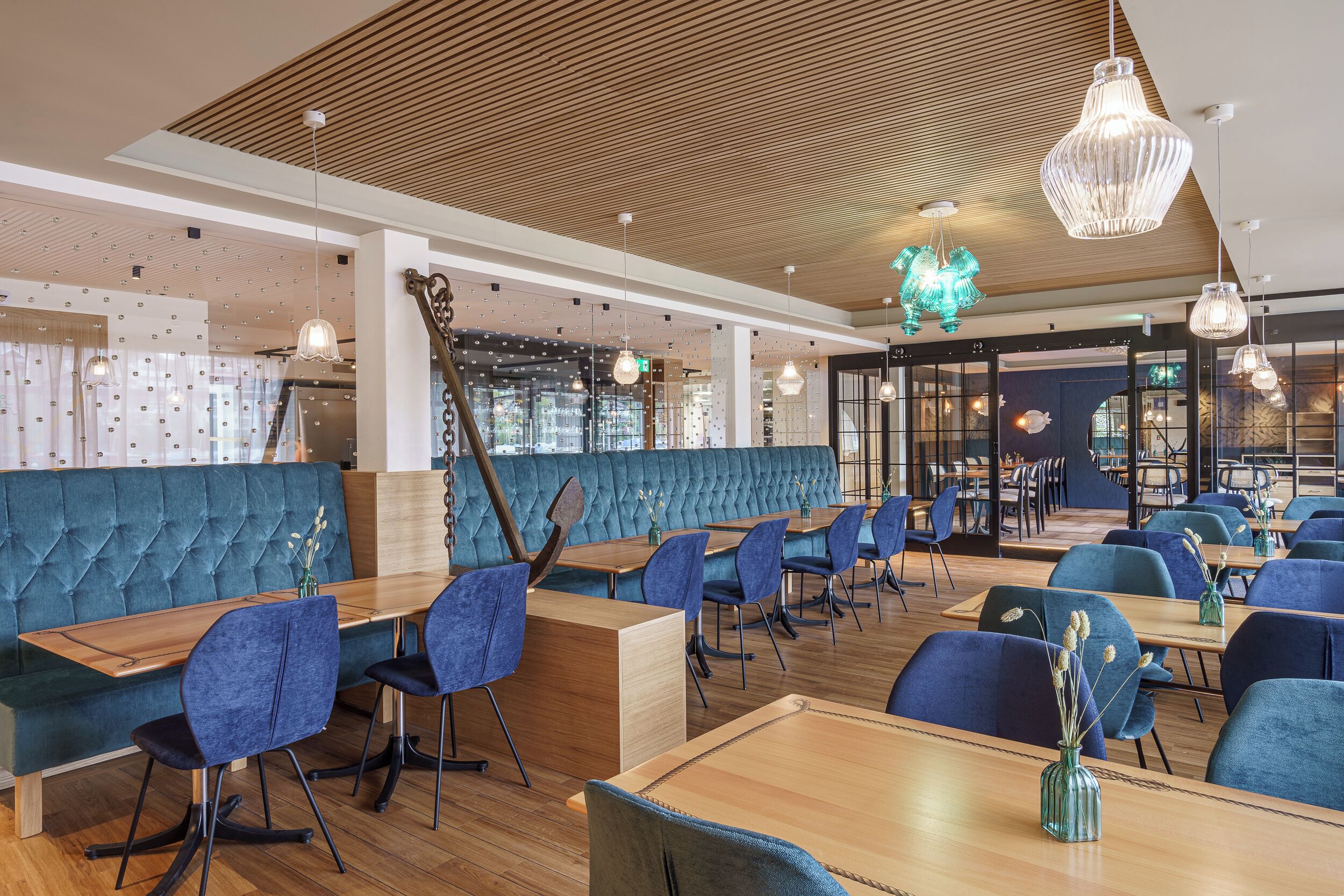 A modern restaurant with a teal upholstered booth, wooden tables, and blue chairs.