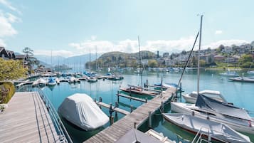 Un puerto deportivo con barcos amarrados, un muelle de madera y un fondo de casas y montañas.