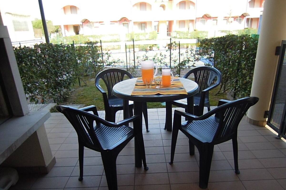 A patio with a round table and four chairs, two glasses of beer, and a small pitcher on a tiled floor.