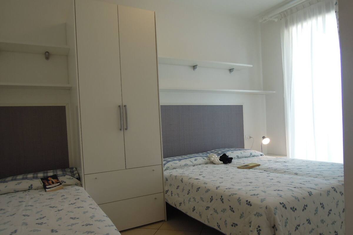 A bedroom with two beds, a wardrobe, and a shelf above the beds.