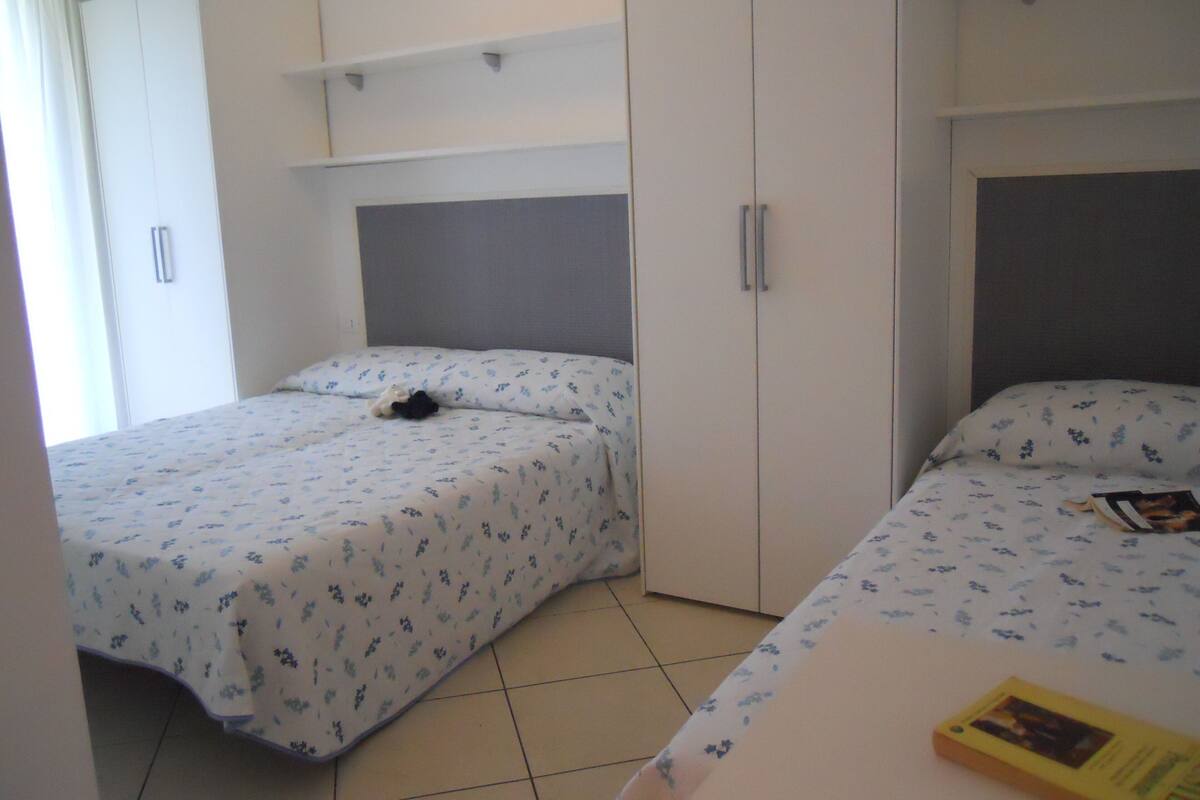 A bedroom with two beds, a wardrobe, and a shelf.