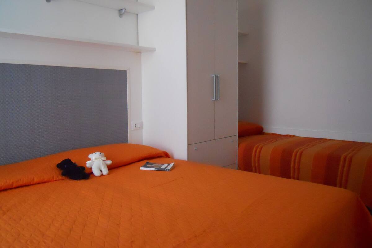 A hotel room with two beds, each with an orange bedspread, a white stuffed toy, and a book on one bed.