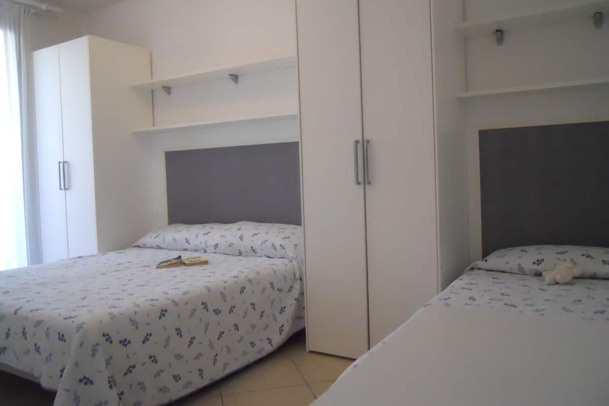 A bedroom with two beds, a wardrobe, and a shelf unit.