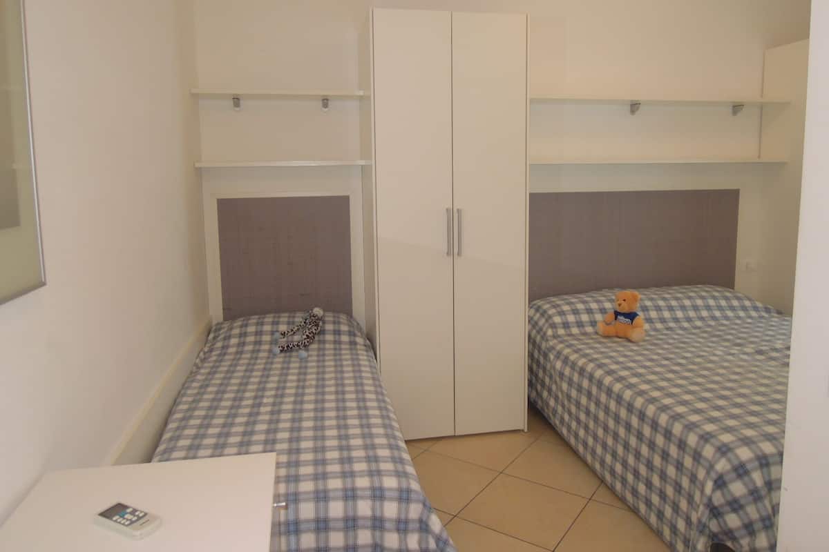 A small, compact room with two single beds, a wardrobe, and a desk with a chair.