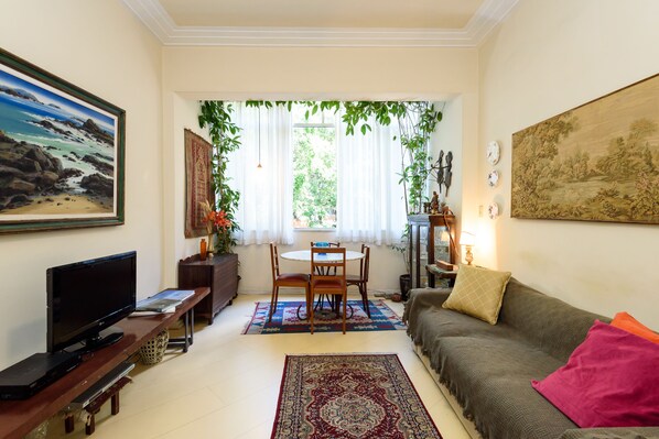 A living room with a TV, sofa, and a dining area with chairs and a table.