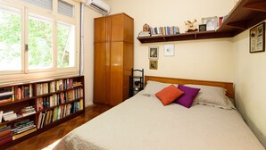 Een slaapkamer met een bed, een boekenkast, een garderobe en een raam met jaloezieën.