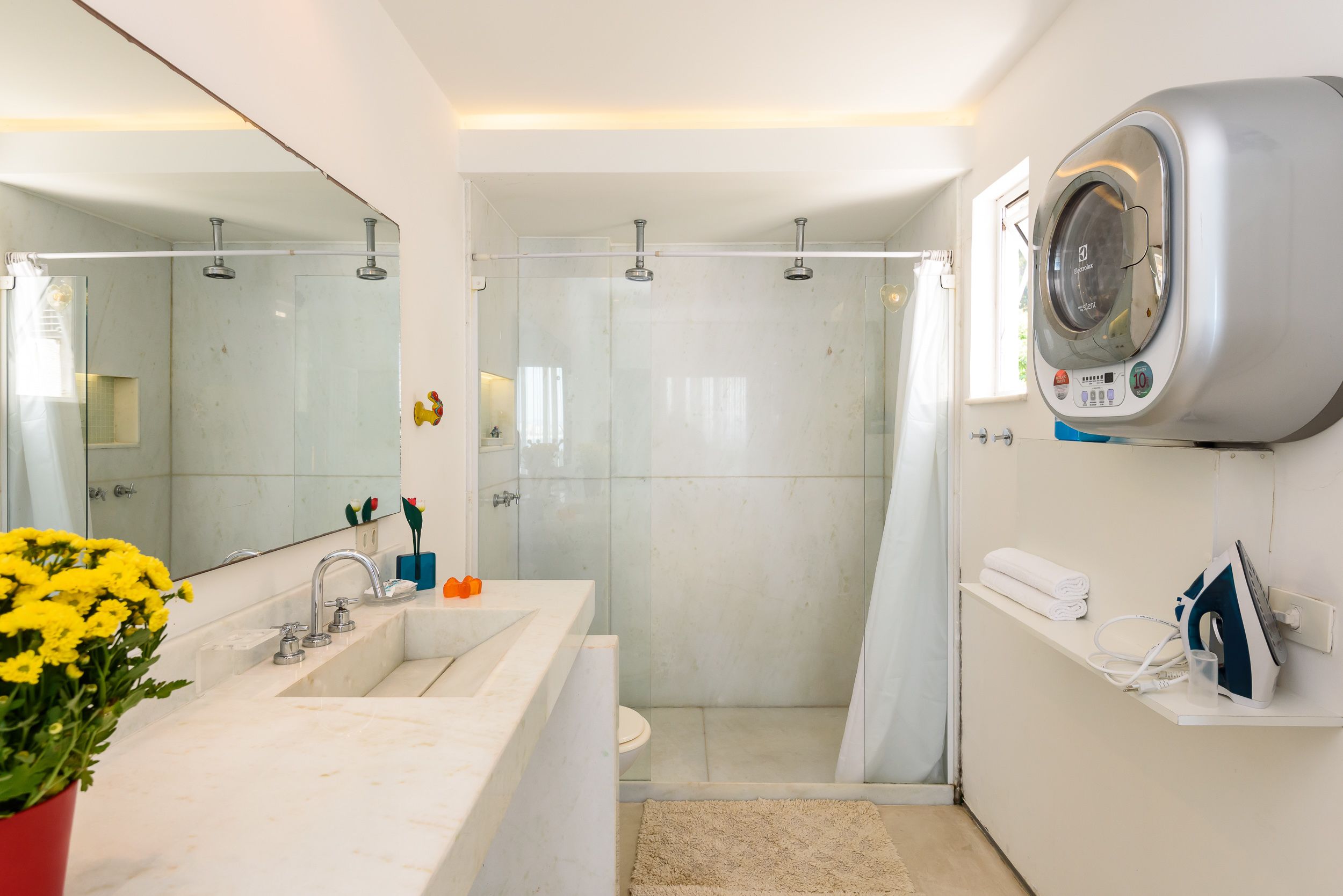 Un baño moderno con un espejo grande, una ducha, lavadora integrada y un lavabo con un florero.