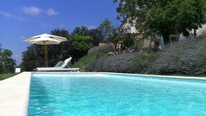 A swimming pool with lounge chairs and an umbrella, surrounded by greenery and a hillside. - La Bastide (Lamillarie)