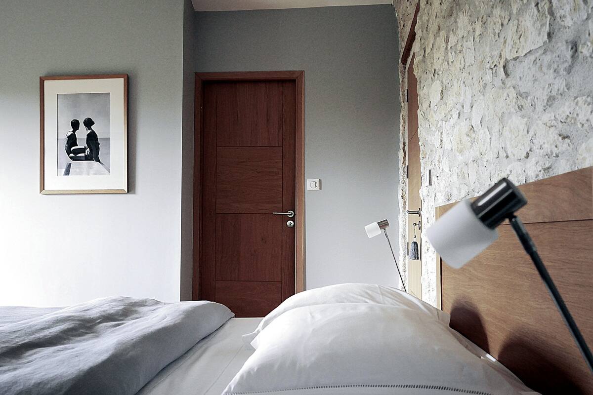 A bedroom with a wooden door, a framed picture on the wall, and a bedside lamp.