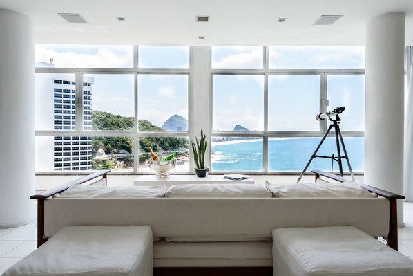 A modern living room with a large window overlooking a beach and cityscape.