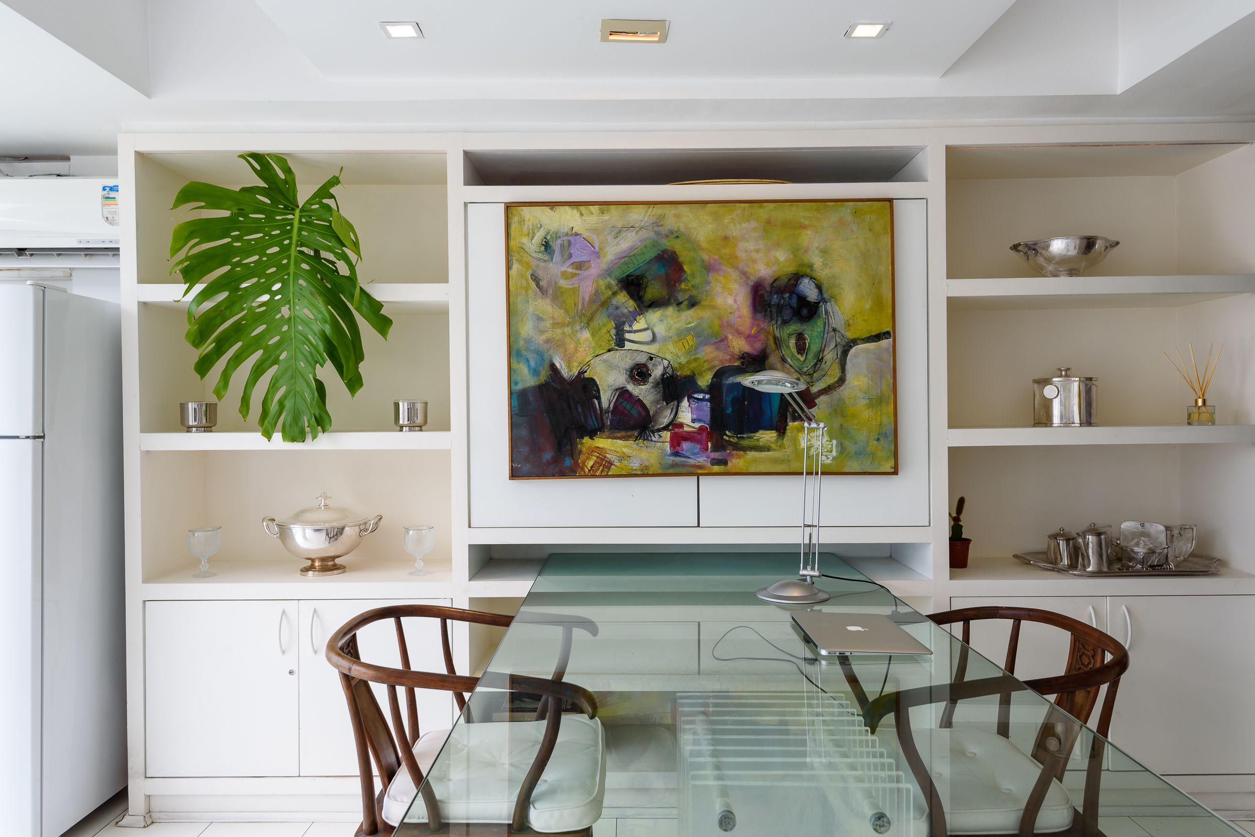 Una cocina moderna con armarios blancos, una mesa de comedor de vidrio y un cuadro abstracto grande sobre el mostrador.
