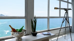 A room with a large window overlooking the sea, a telescope on a tripod, a silver bowl with bottles, and a potted plant. - Omar do Rio - Apartamento V902 (Rio de Janeiro)