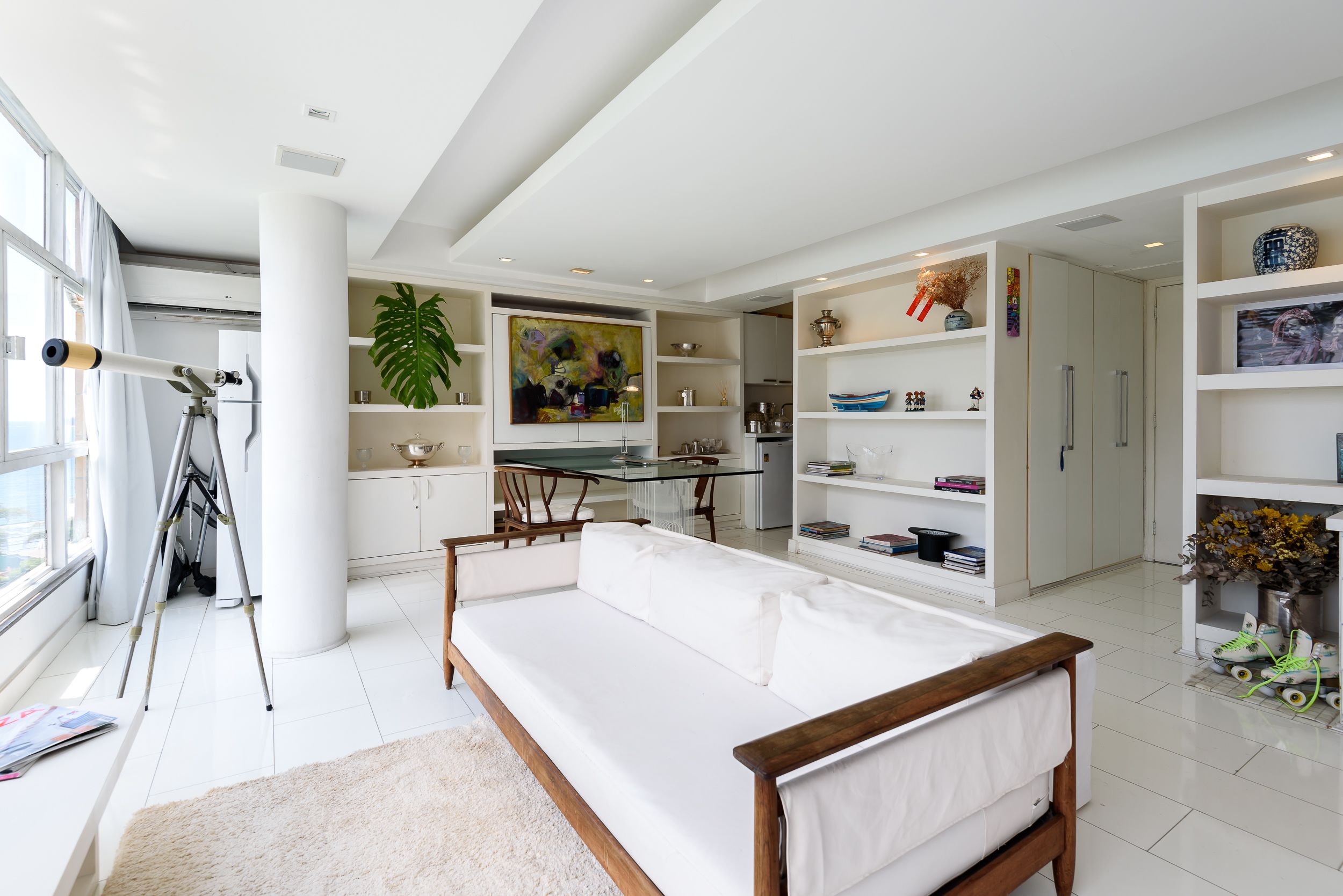 A modern living room with a white sofa, a dining area with a glass table, and a kitchen with white cabinets.
