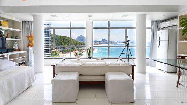 A modern living room with a large window offering a view of the ocean and mountains. - Omar do Rio - Apartamento V902 (Rio de Janeiro)