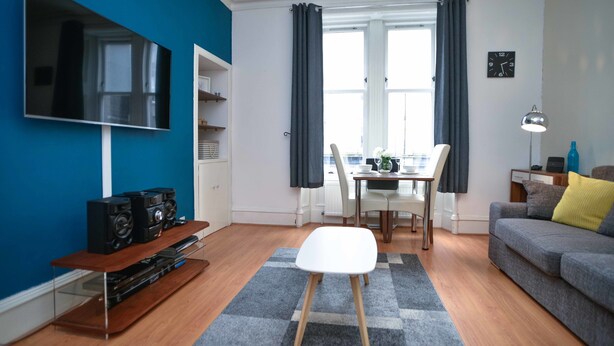 A living room with a flat-screen TV, a coffee table, a sofa, and a dining area with chairs and a table.