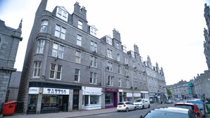 A multi-story building with various storefronts, including a tattoo parlor and a hair salon.