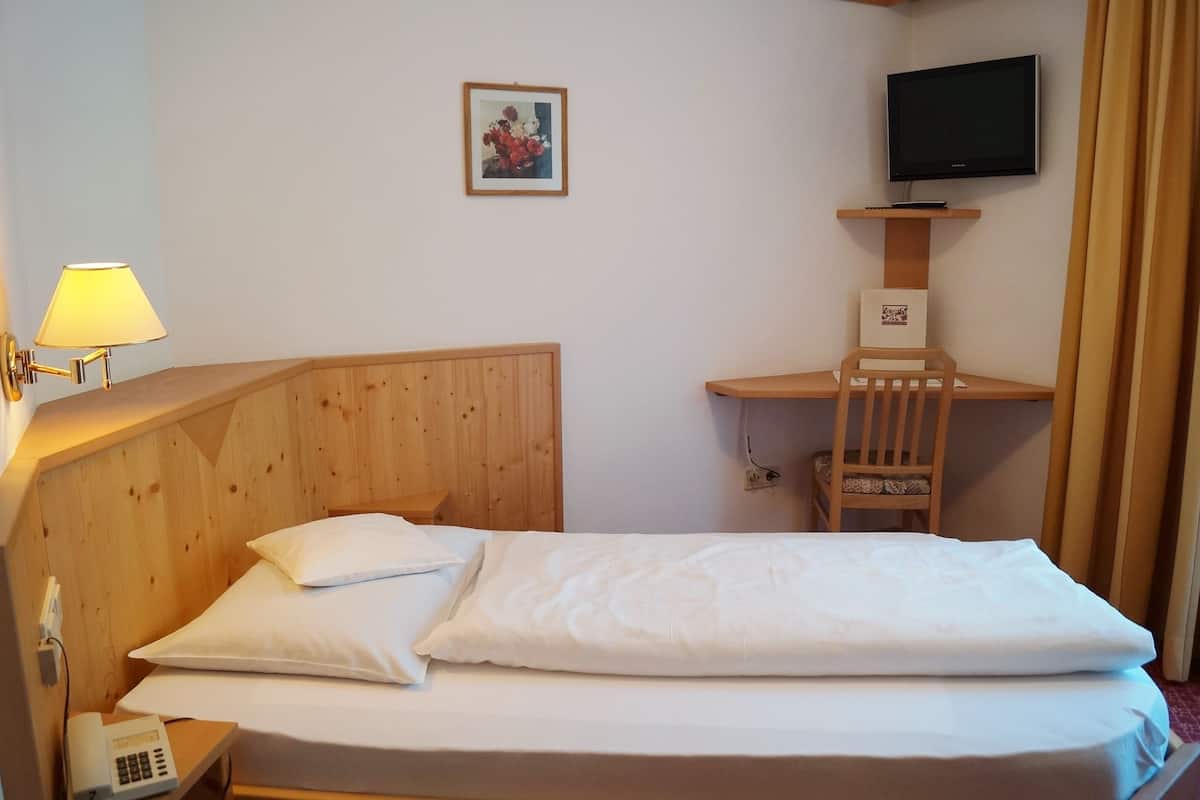 Ein Hotelzimmer mit einem hölzernen Bett, einer Nachttischlampe, einem Schreibtisch mit Stuhl, einem Fernseher und einem gerahmten Bild an der Wand.
