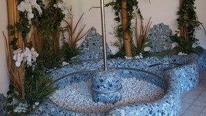 A mosaic bench with a central pole, surrounded by white flowers and greenery. - Gasthof Laurin (Tires)