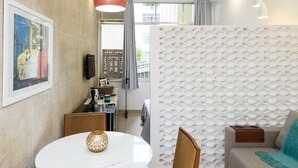 A modern living room with a round white table, wooden chairs, a beige sofa, and a decorative wall panel.