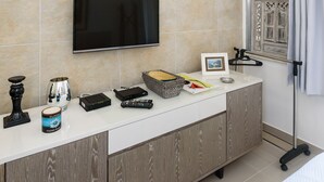 A modern bathroom with a large mirror, a mounted television, and a vanity with a sink and storage.