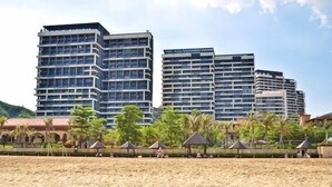 Un hotel frente a la playa con edificios altos, palmeras y sombrillas.