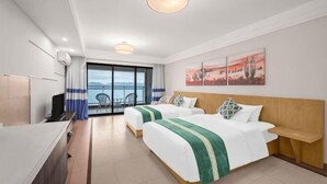 Habitación de hotel con dos camas, un escritorio, televisión y balcón con vistas.