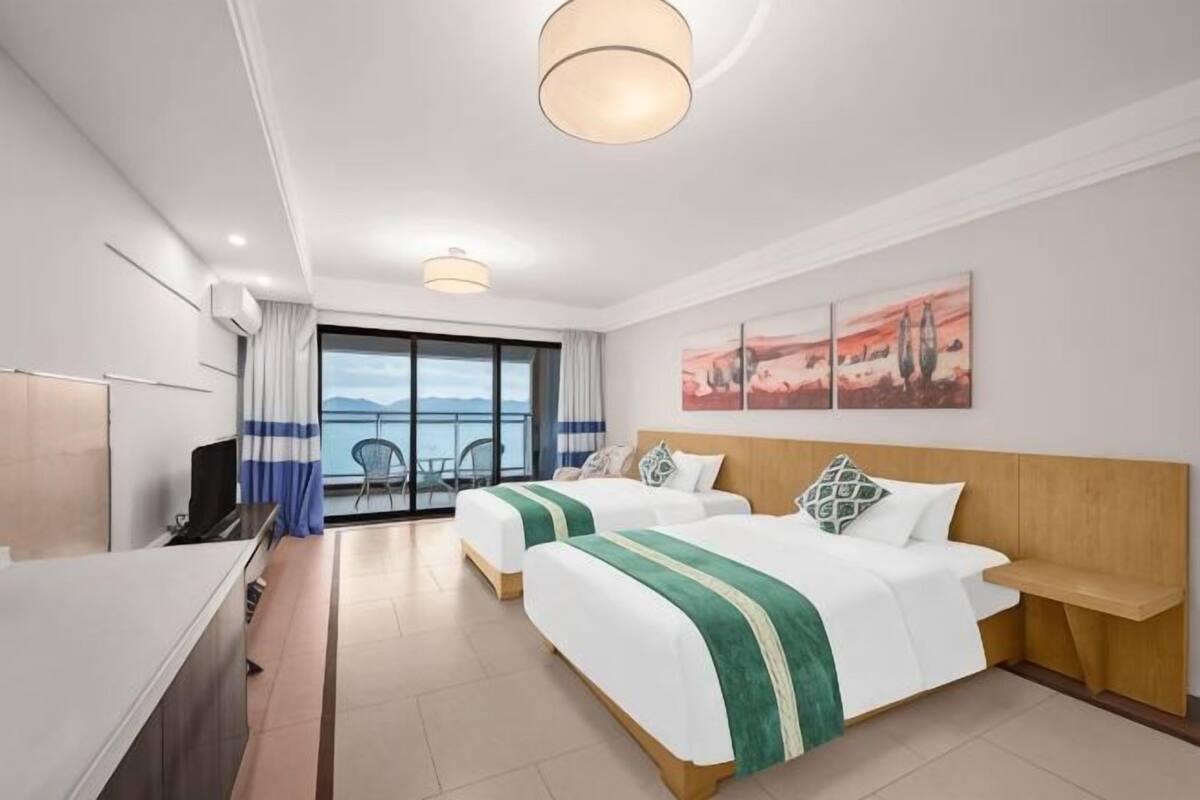 Quarto de hotel com duas camas, uma mesa, uma televisão e varanda com vista.