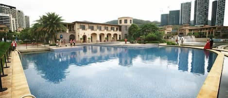 A swimming pool with a tiled edge, surrounded by a building with arched windows and a palm tree.