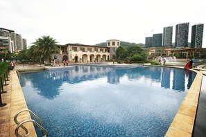 Une piscine dont le bord est revêtu de carreaux, entourée d’un bâtiment doté de fenêtres en arc de cercle et d’un palmier.