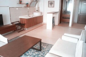 Uma sala de estar moderna com sofá, mesa de centro, TV, área de cozinha com pia e bancada, e um tapete estampado.