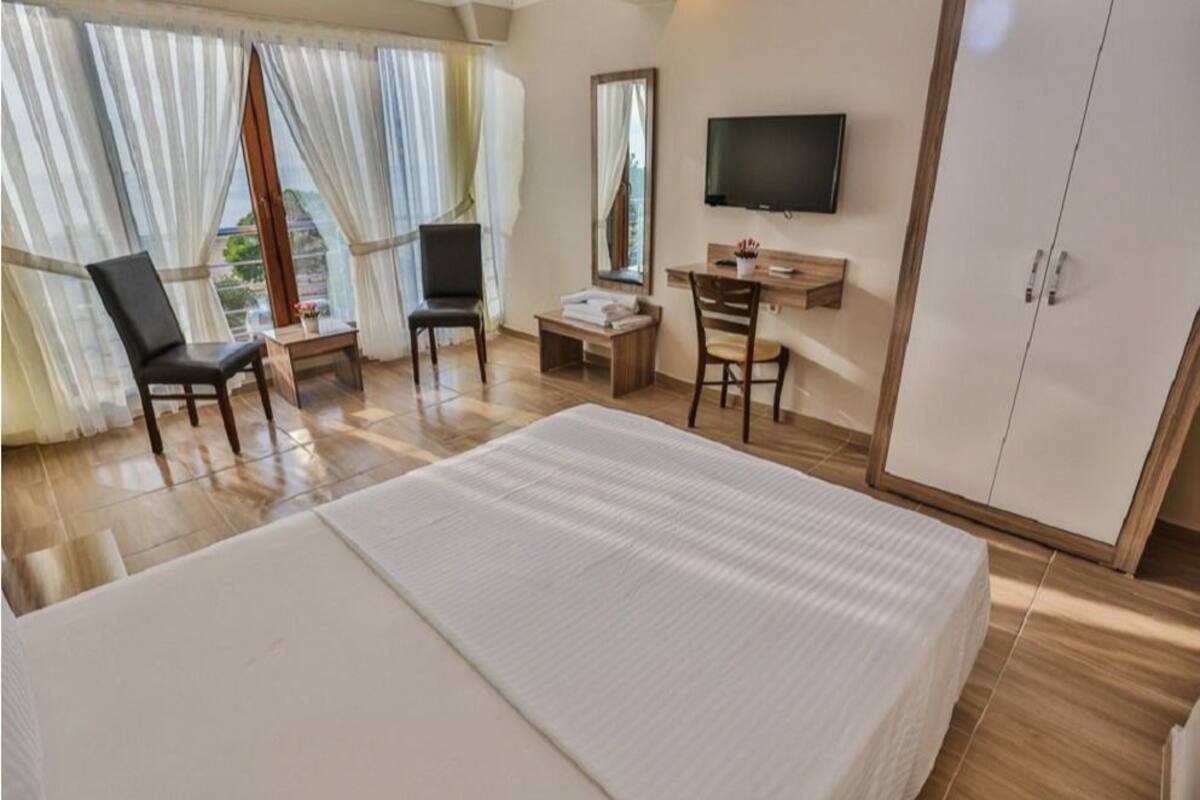 A hotel room with a large bed, two chairs, a desk, a television, and a wardrobe.