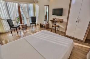 A hotel room with a large bed, two chairs, a desk, a television, and a wardrobe.