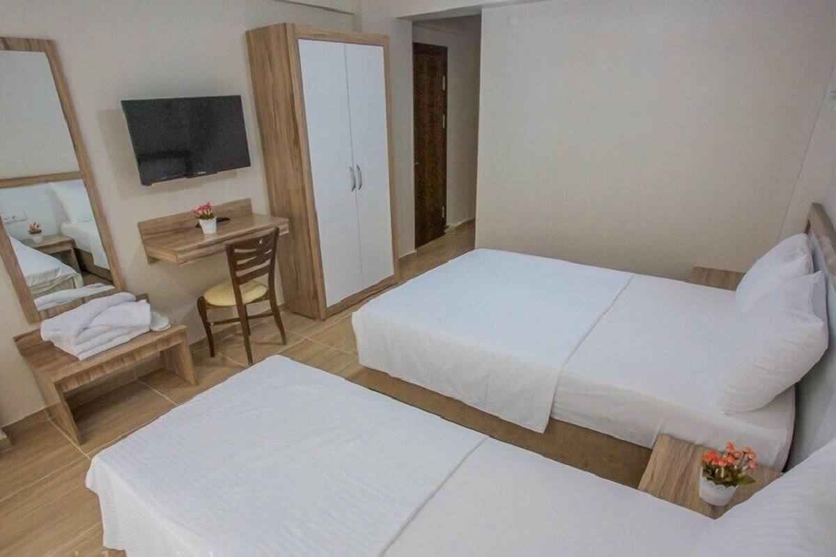 A hotel room with two beds, a desk with a chair, a TV, and a wardrobe.
