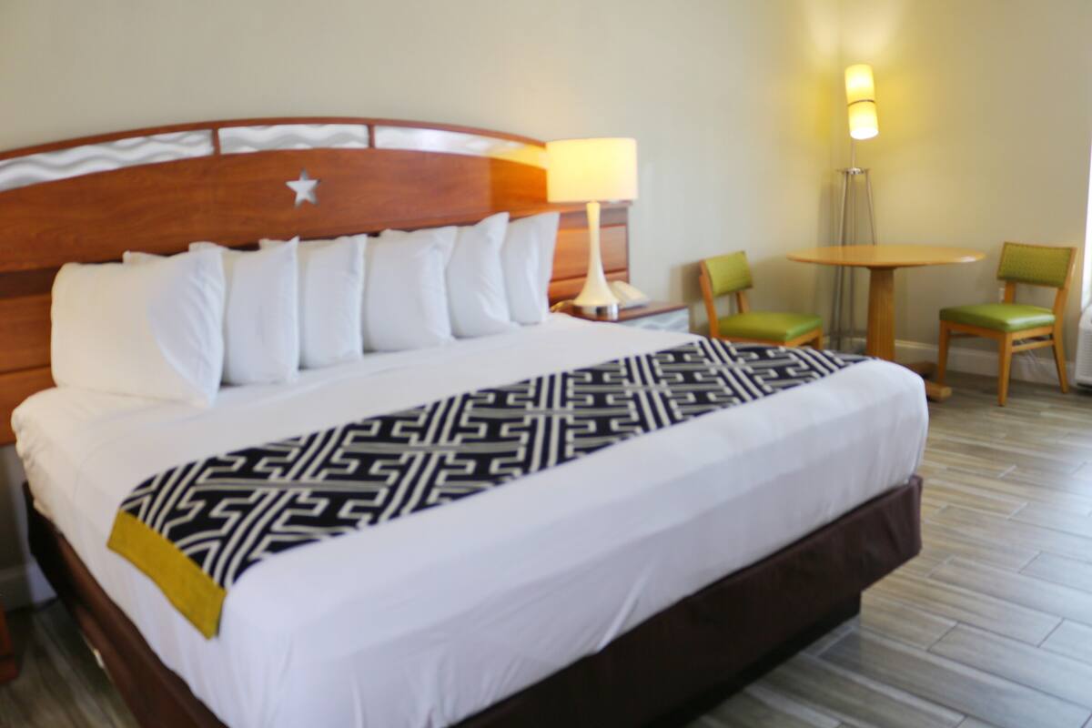 A hotel room with a large bed, a nightstand, a lamp, two chairs, and a small table.
