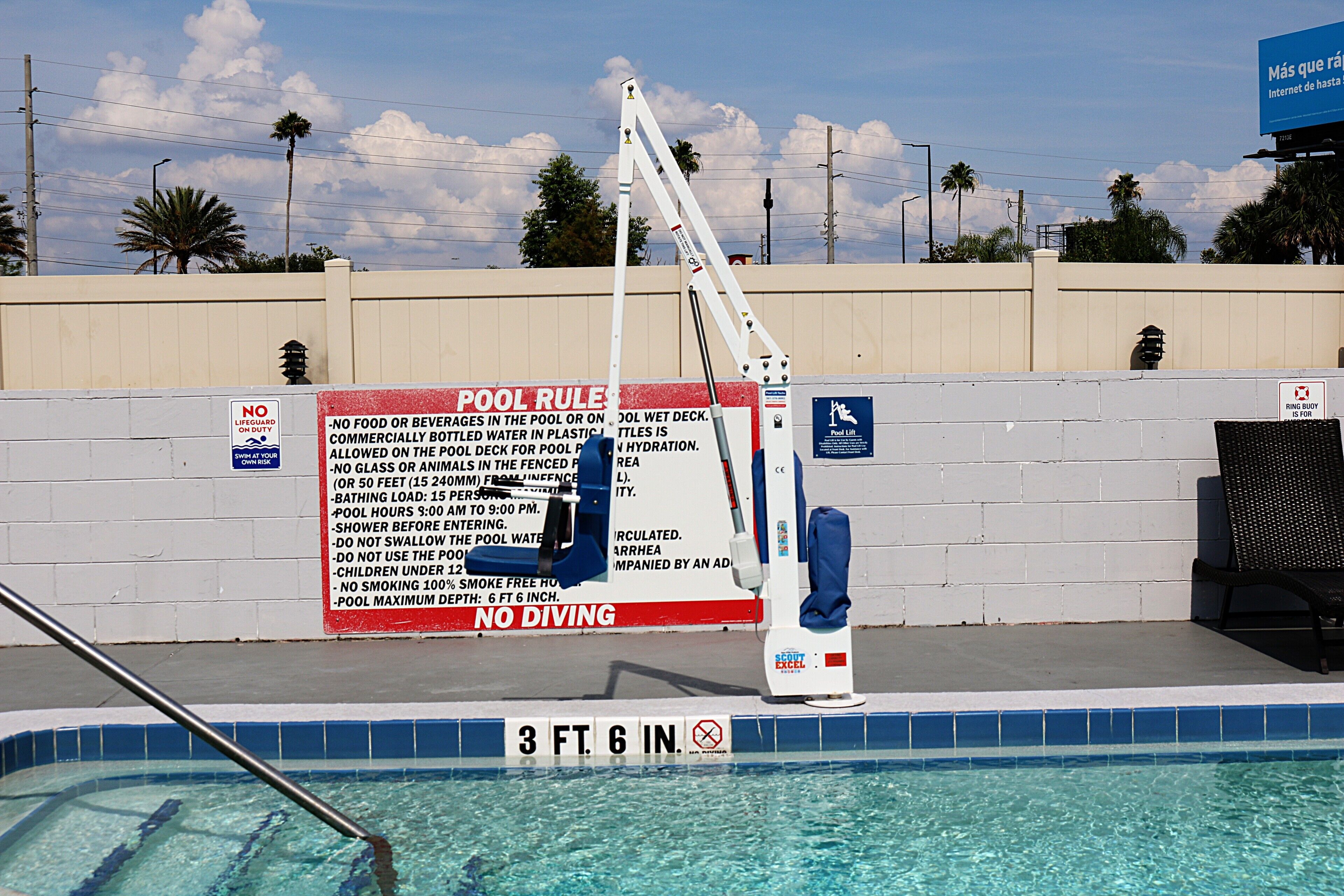 Una piscina con un cartel de prohibido sumergirse, un puesto de socorrista y un letrero con las normas de la piscina.