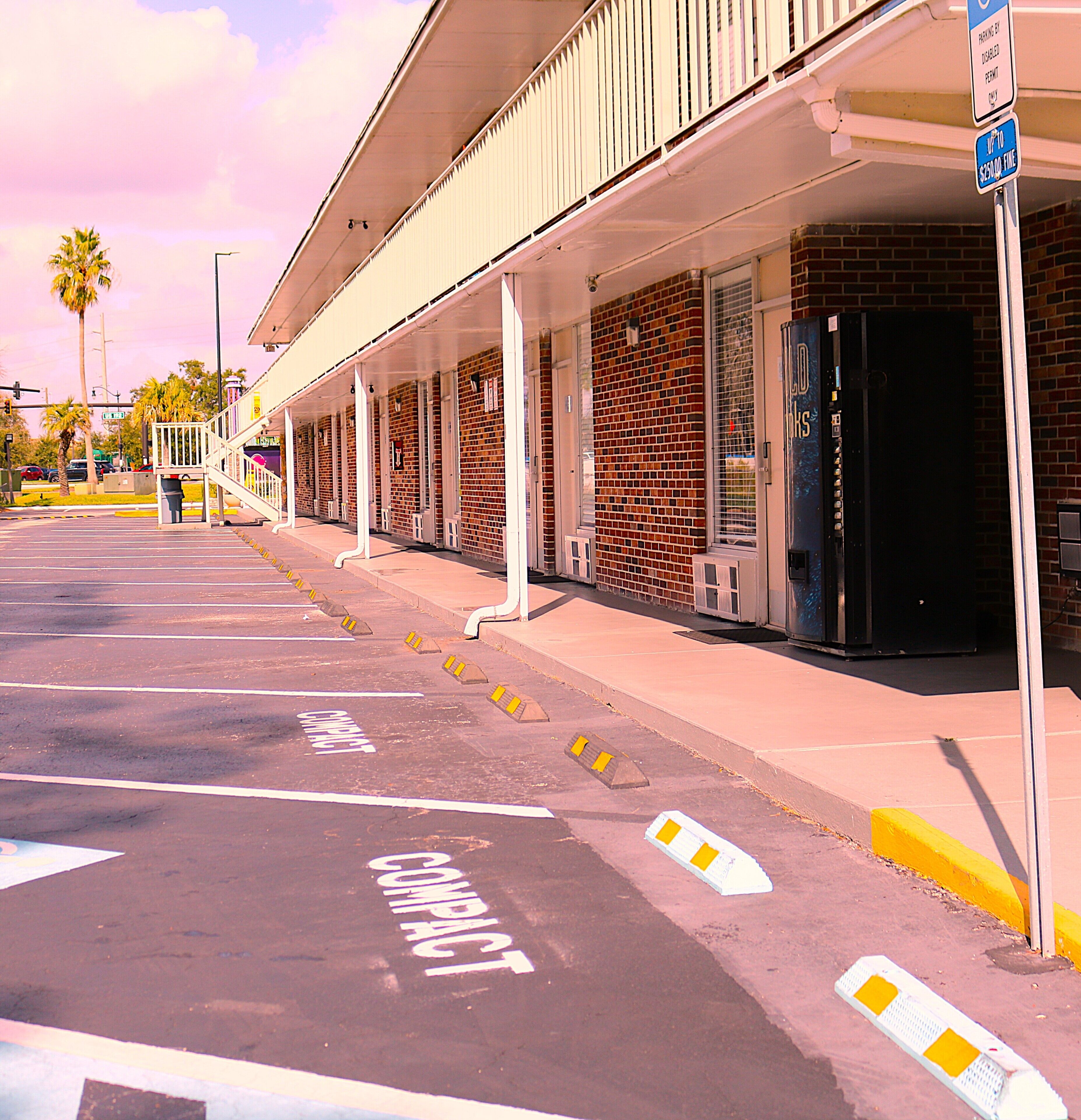 A parking lot with marked compact parking spaces and a building with a brick facade.