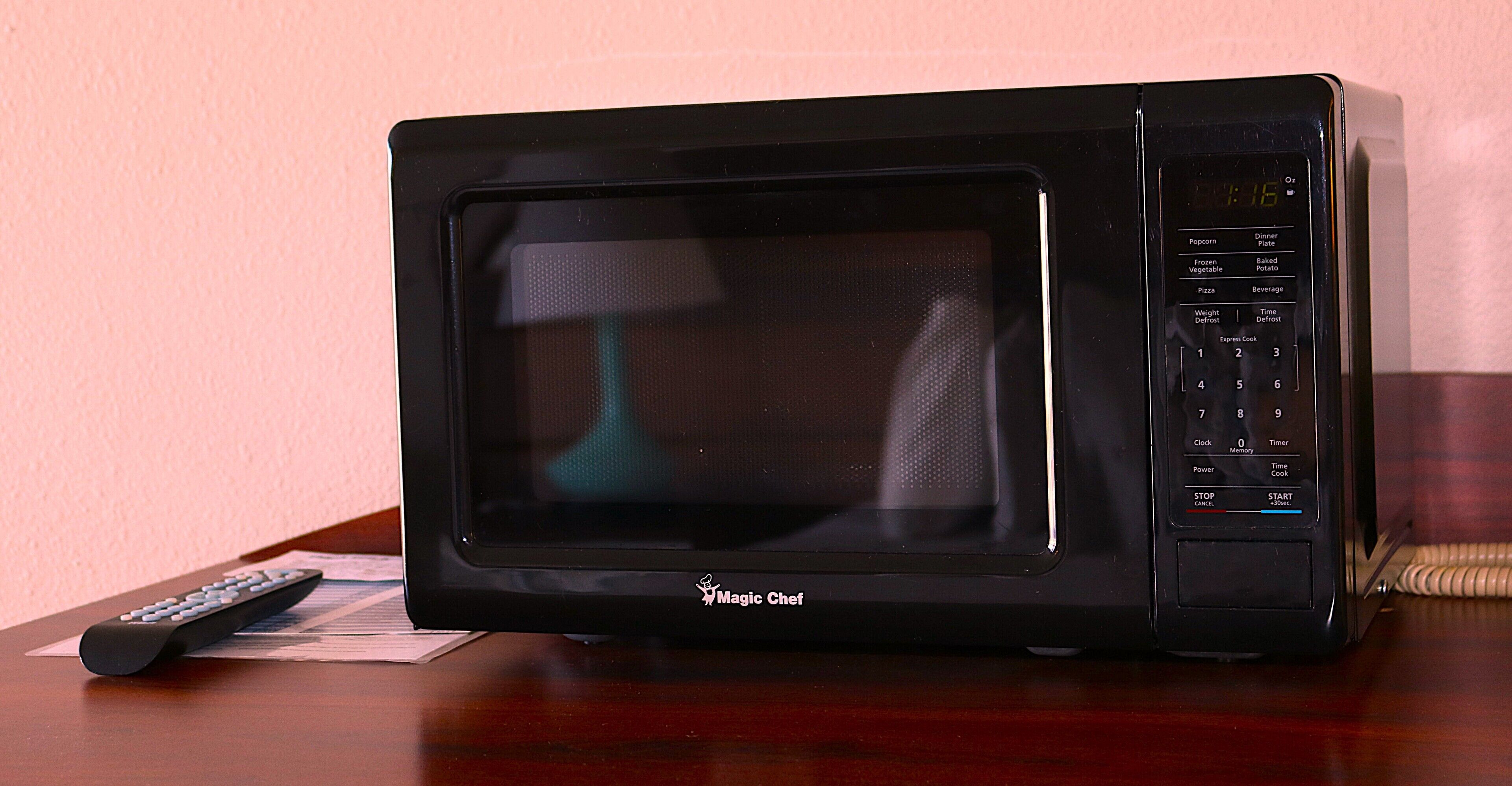 Un forno a microonde nero con display digitale e telecomando su un tavolo di legno.
