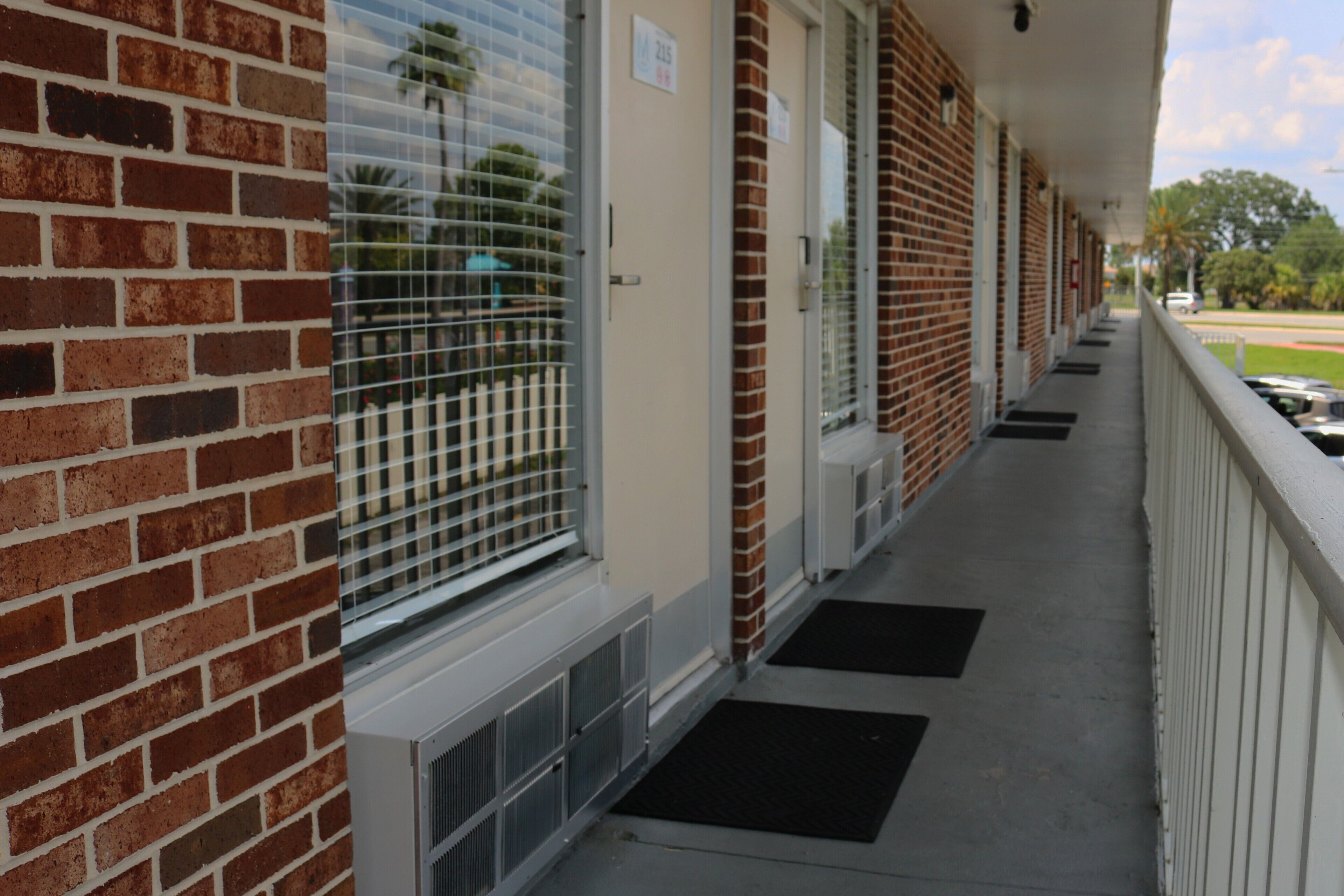 A brick building with a covered porch, numbered doors, and a clear view of the street.