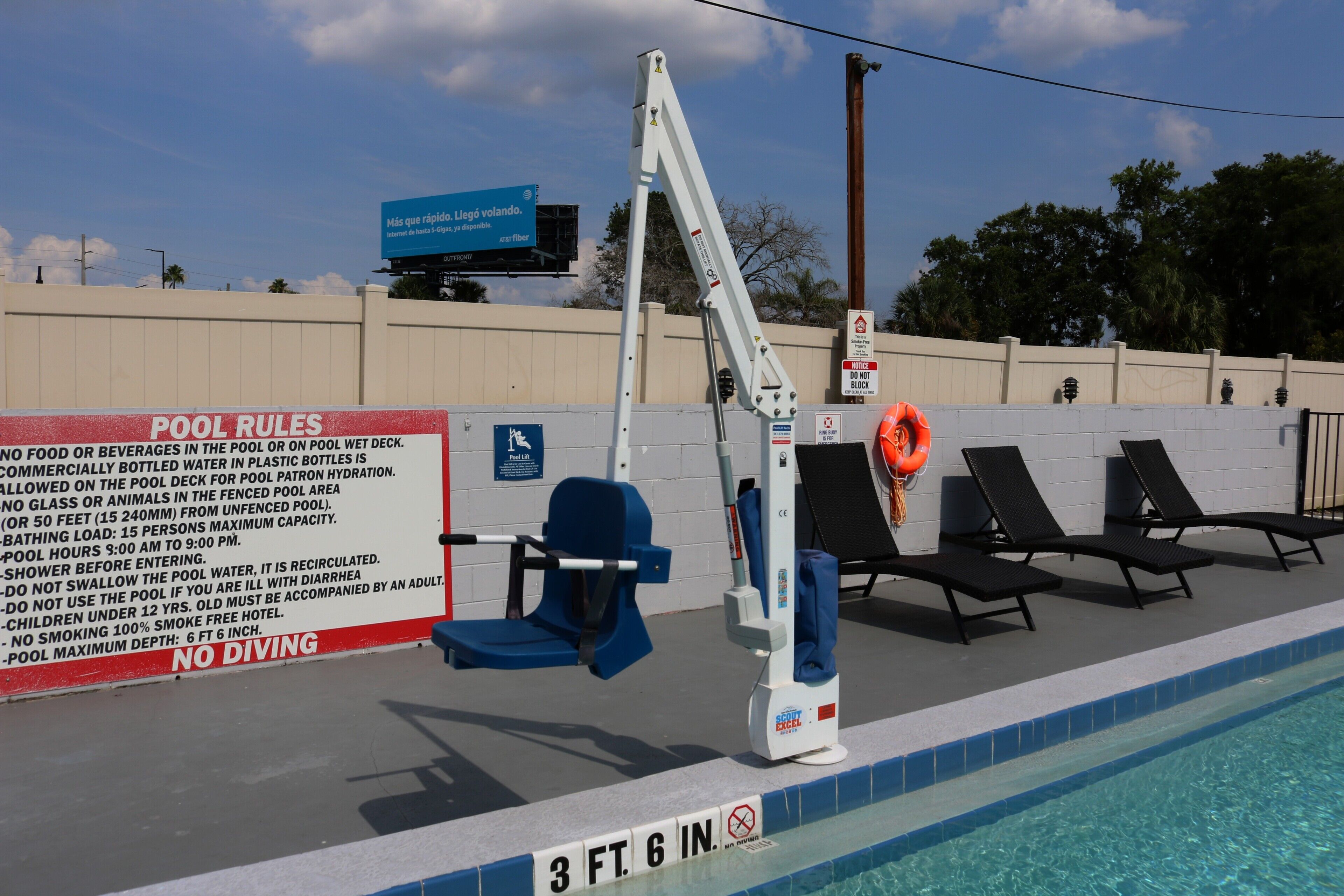 A pool area with a sign detailing pool rules, a lifeguard chair, lounge chairs, and a pool depth marker.