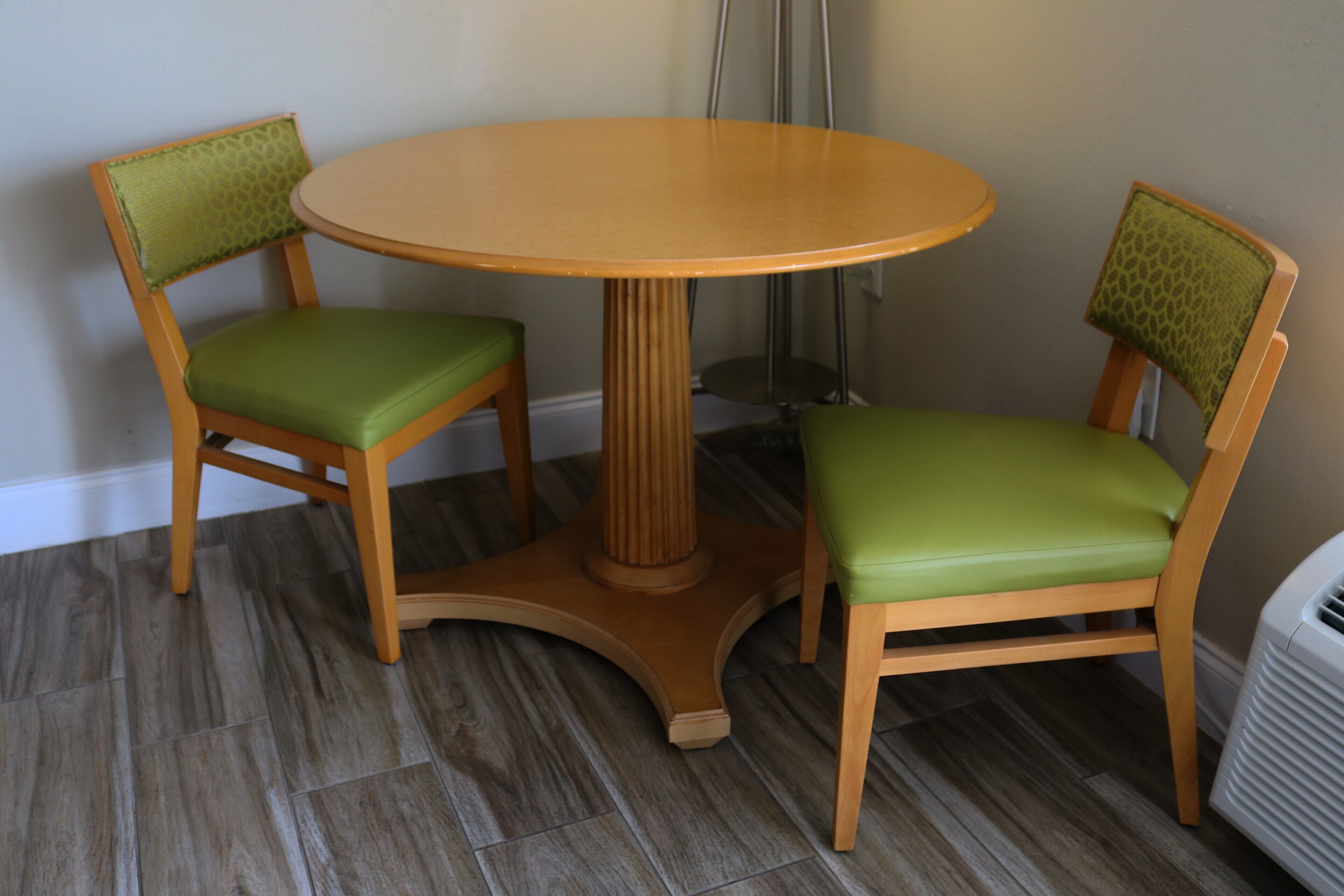 Une table ronde en bois, accompagnée de deux chaises vertes à coussin.