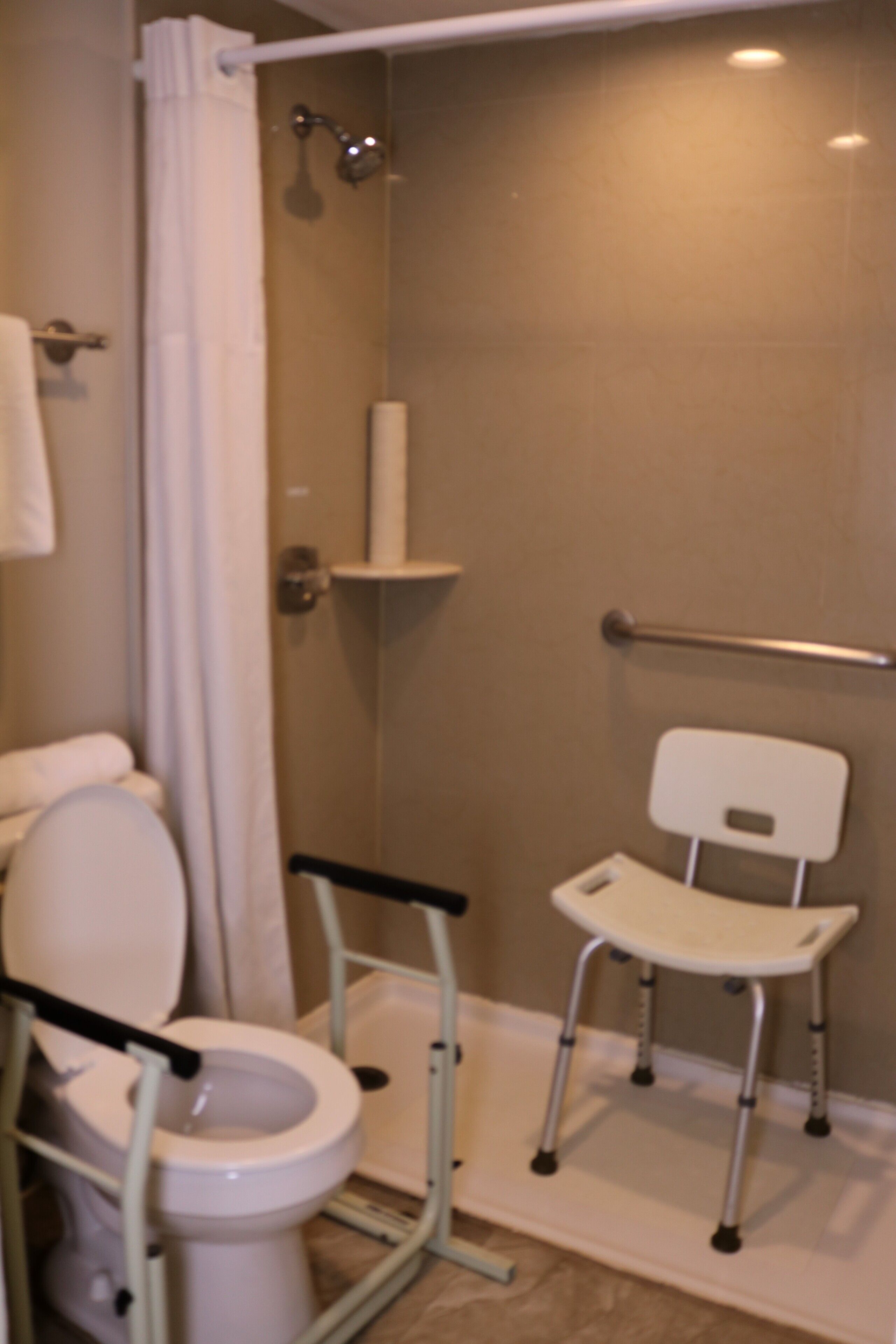 Une salle de bain équipée de toilettes accessibles aux personnes en fauteuil roulant, d’une douche et d’une barre d’appui.